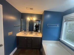 Freshly painted blue bathroom with double-sink vanity, dark cabinets, large mirror, and white soaking tub