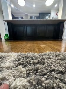 Freshly painted black kitchen island with raised panel sides, granite countertop, hardwood flooring, and shag area rug