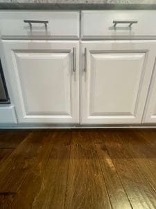 Freshly painted white kitchen base cabinets with raised panel doors, brushed nickel handles, and hardwood flooring