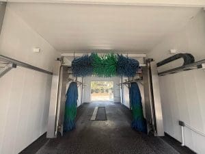 Interior of an automatic car wash bay with blue and green spinning brushes and freshly painted white walls and ceiling
