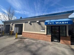 Freshly painted exterior of a Pet Wash and self-service car wash building with gray stucco, red brick base, and blue awning