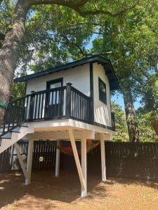 Freshly painted Charleston SC backyard playhouse with white siding and black trim, raised on stilts