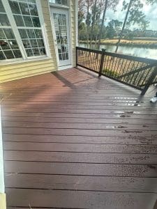 Freshly stained Charleston SC backyard deck with rich brown boards, black railings, and lakefront view