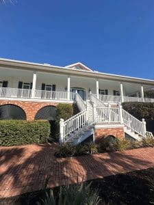 Freshly painted Charleston SC home exterior with white siding, black shutters, brick base, and dual front staircases