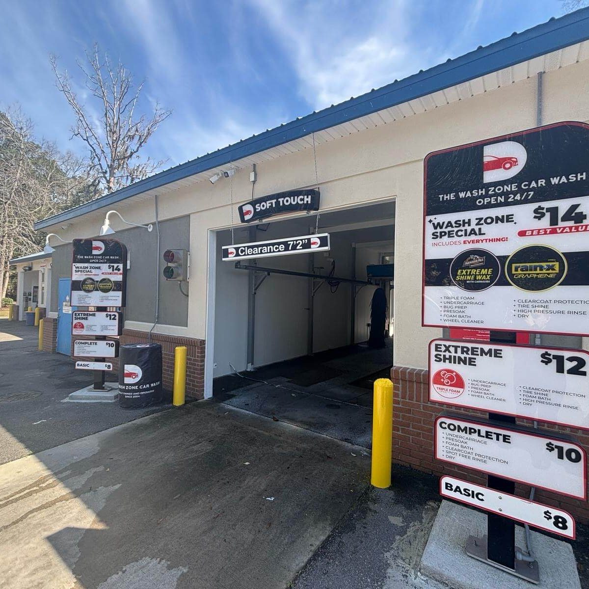 Freshly painted exterior of The Wash Zone Car Wash with Soft Touch bay, pricing signs, and tan stucco walls with red brick base