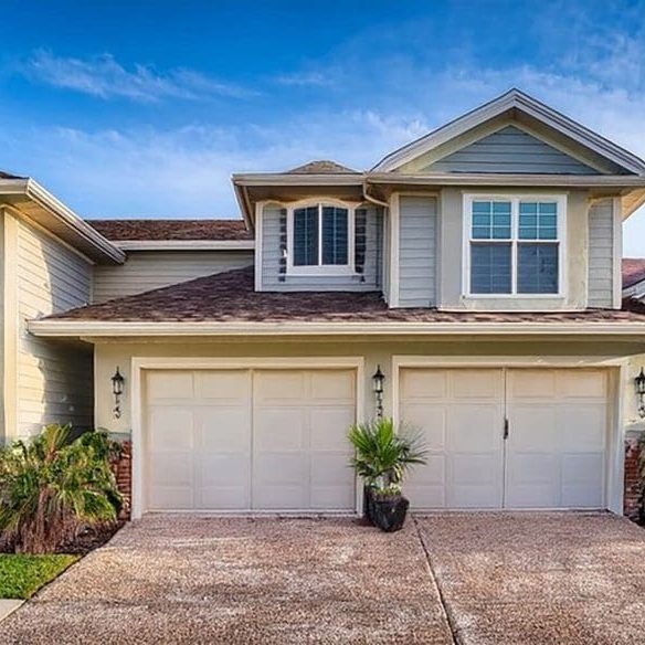 Freshly painted two-story Charleston SC home with cream siding, double garage, and tropical landscaping